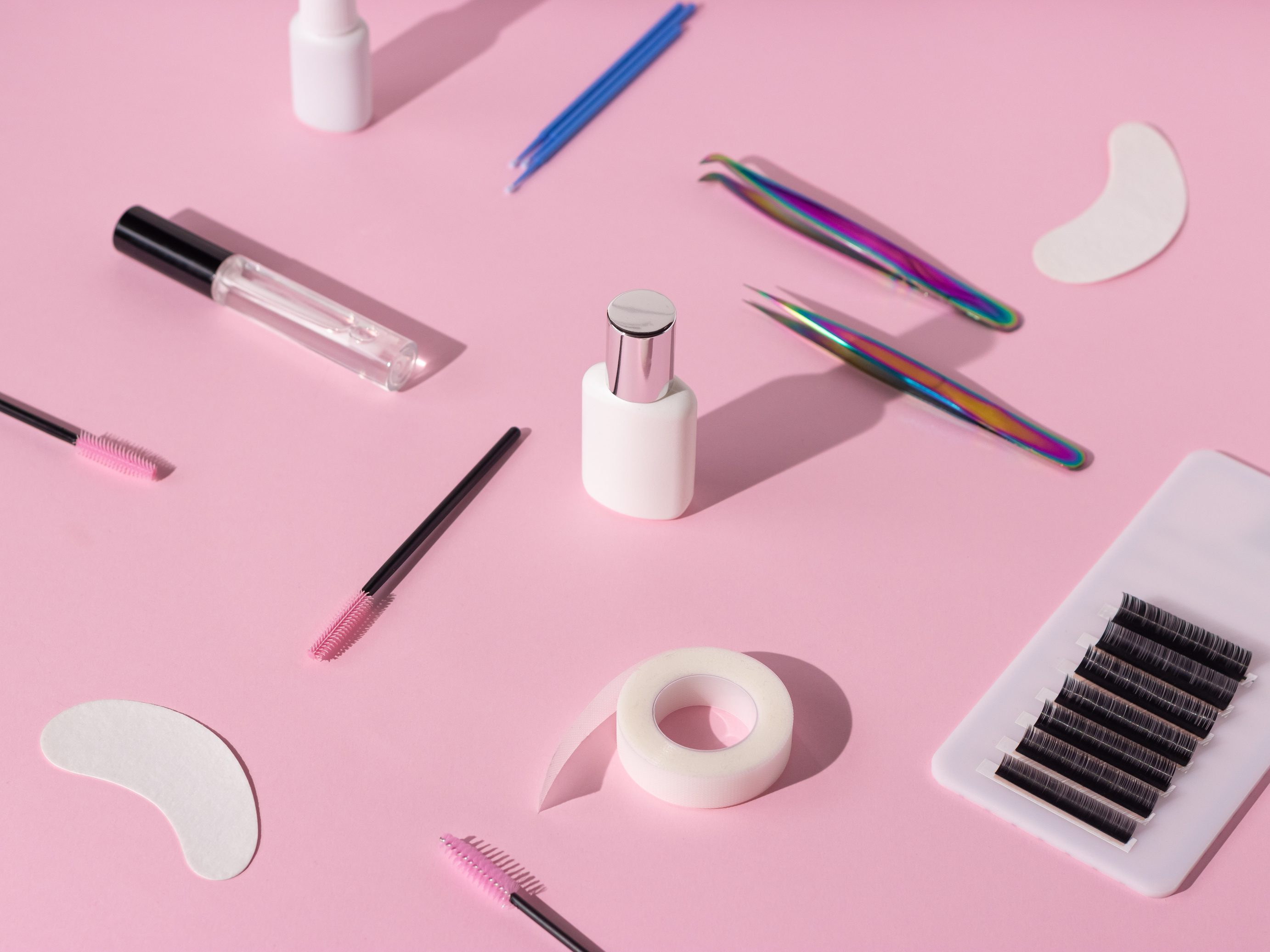 Things for the work of lash-makers, artificial eyelashes, microbrachis, glue, tweezers, combs, brushes for eyelash extensions. Eyelash extension, painting of eyebrows. Pink background.